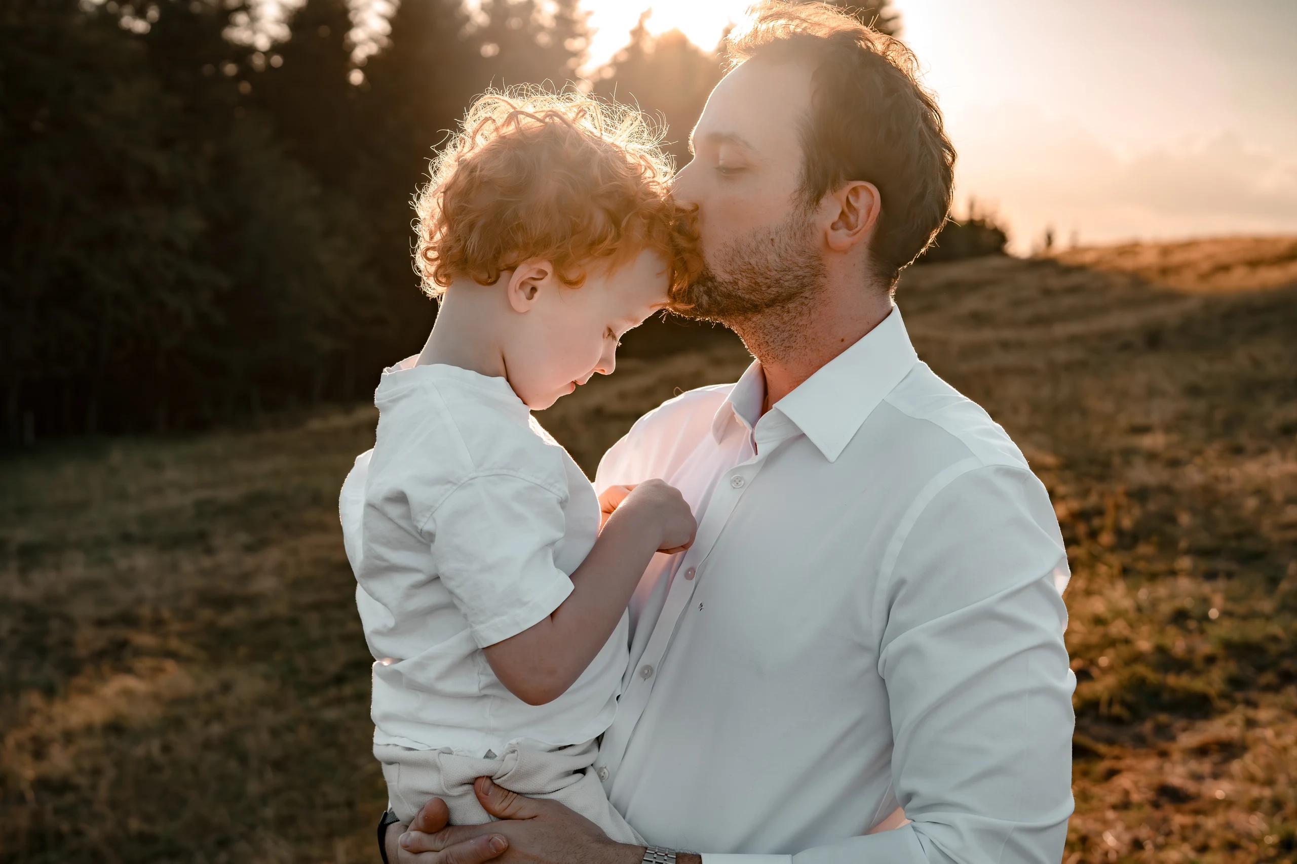 Vater küsst sein Kind liebevoll auf die Stirn im warmen Sonnenuntergang