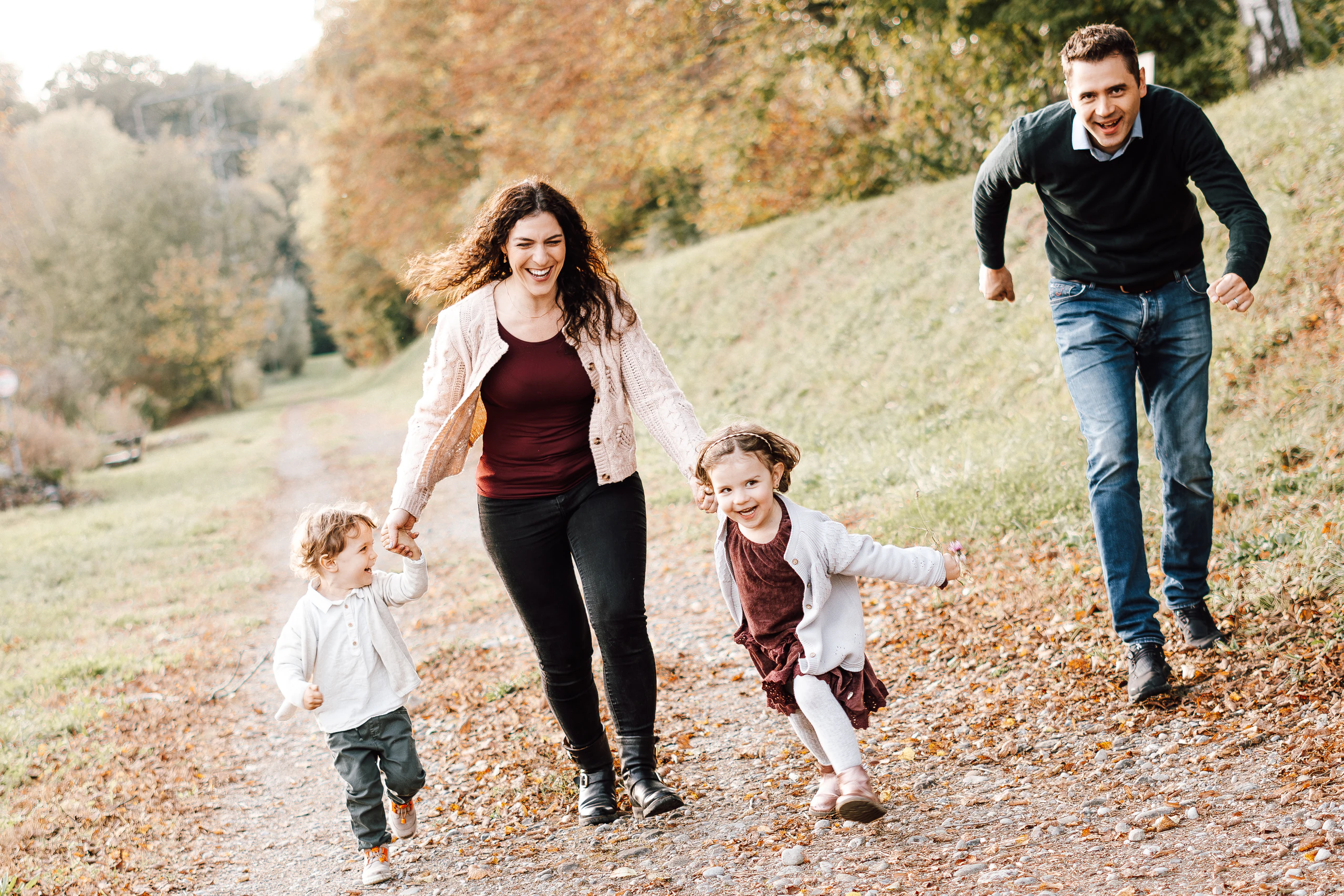 Familie läuft lachend Hand in Hand durch die herbstliche Natur